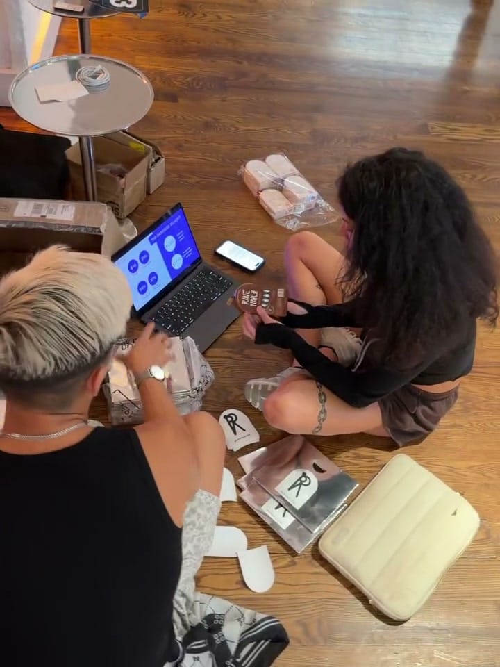 Braelinn Frank and a teammate sitting on the floor packing Rave Nailz orders